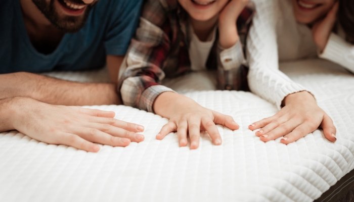Three sets of hands press onto a white mattress.