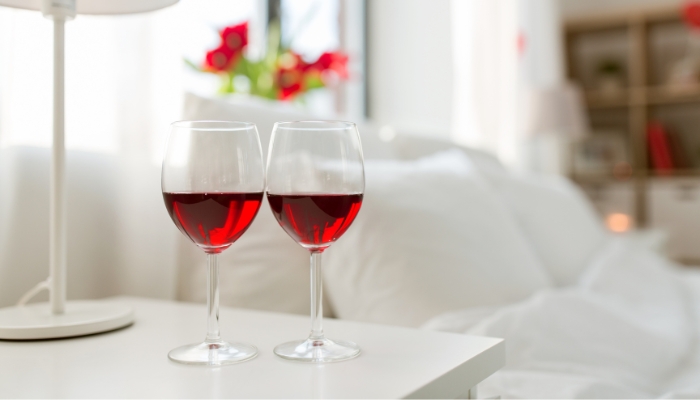 two wine glasses filled with red wine on bedside table
