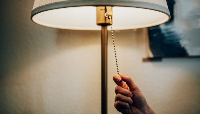 image of a hand reaching to turn off lamp on bedside table in a darkened room