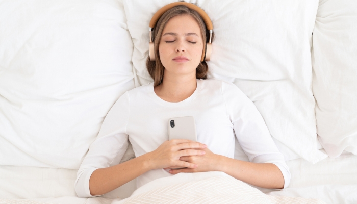 woman in bed sleeping with headphones on while holding smartphone