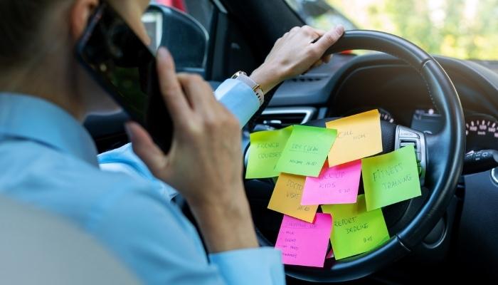 Woman driving while on the phone and tons of sticky note reminders on the steering wheel