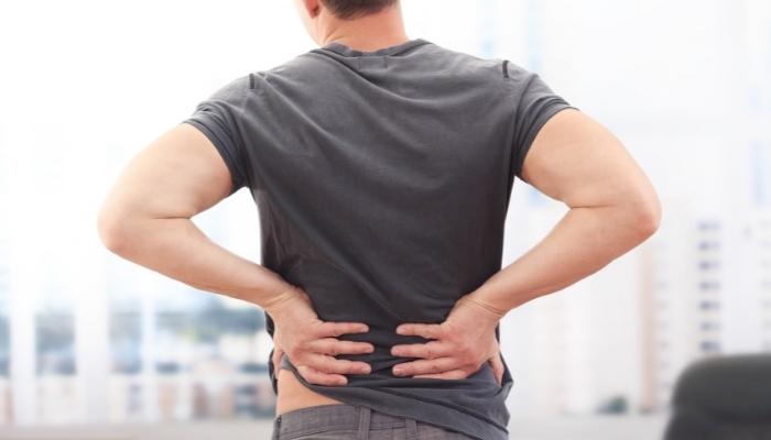 Man in a gray shirt holds his lower back as if in pain