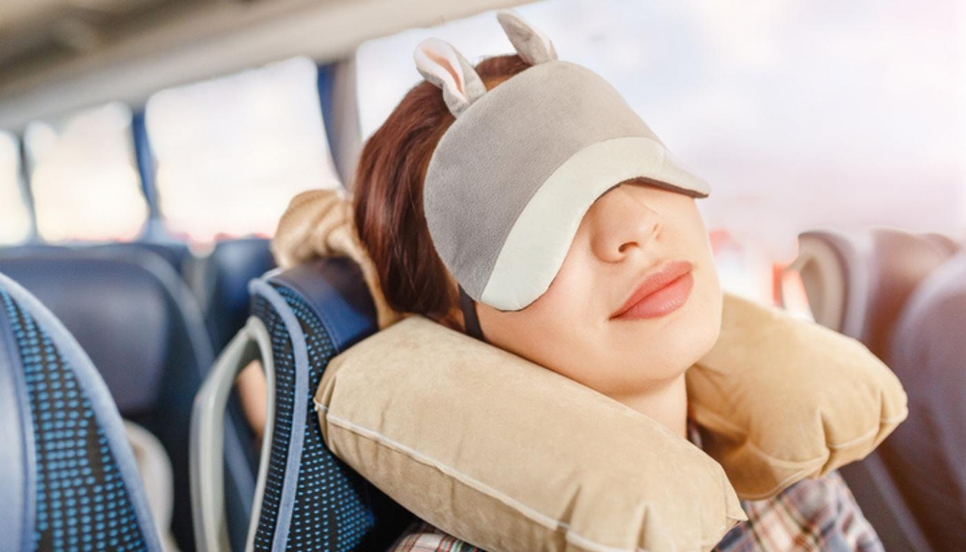 Woman in sleep mask and with pillow travelling on bus