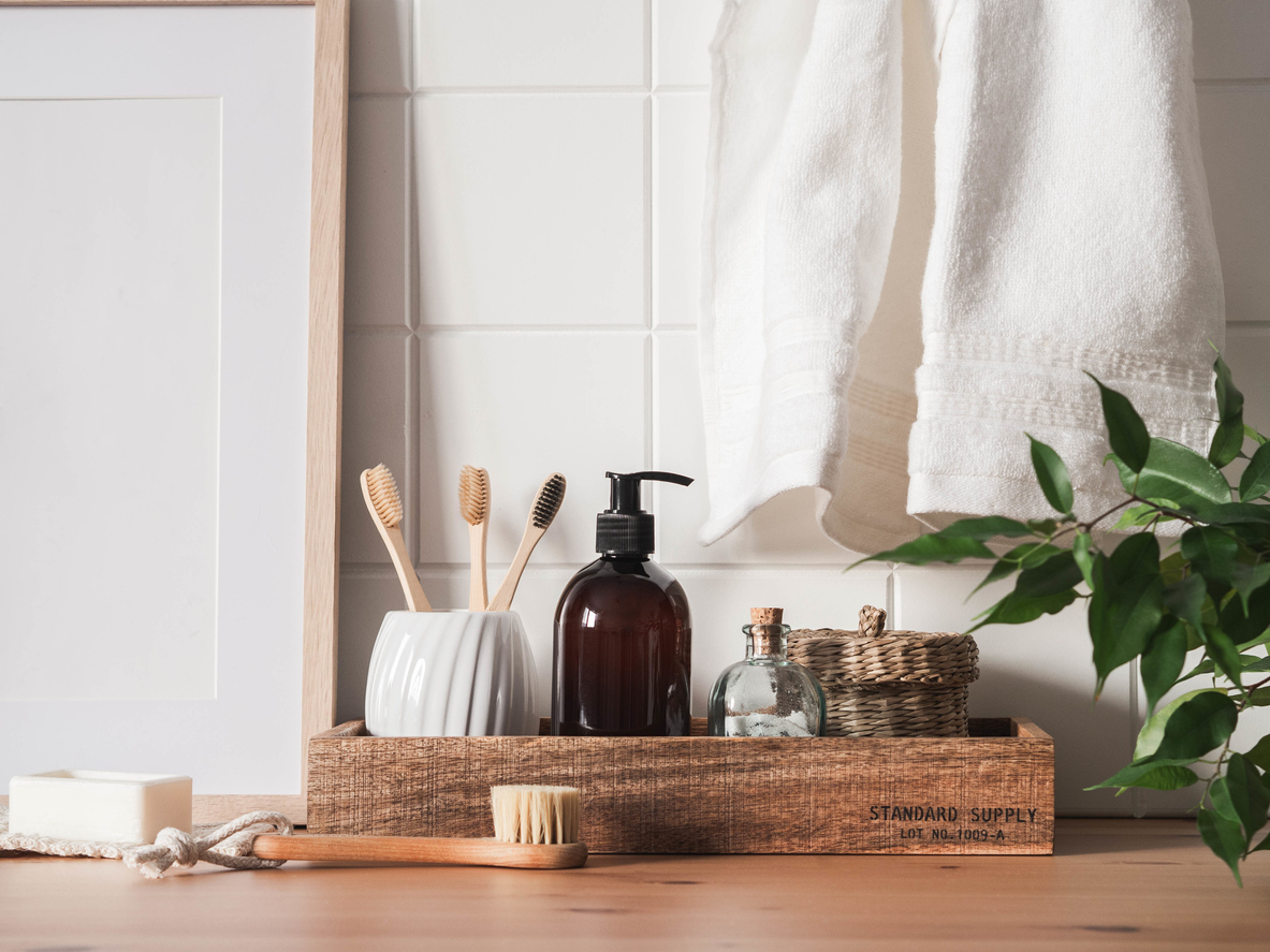 cosmetic bottle, bath accessories, toothbrushes in a glass and houseplants on wood shelf and wall tiles