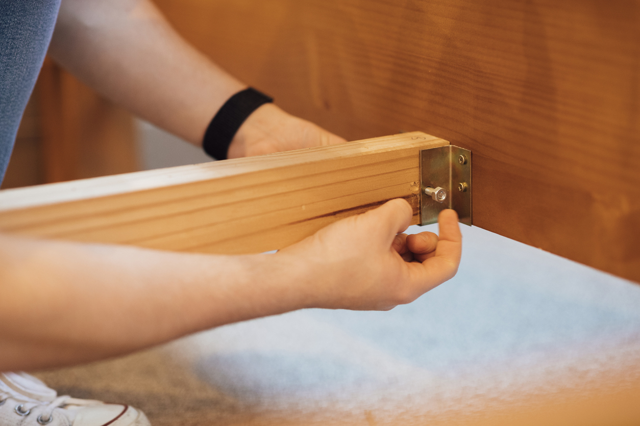 man using his hands to tighten up a bolt while assembling his bed frame