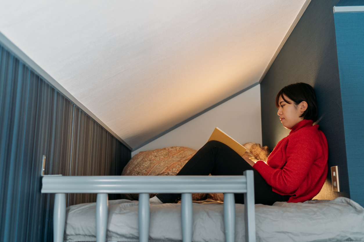 A young woman reads in her loft bed with a full mattress