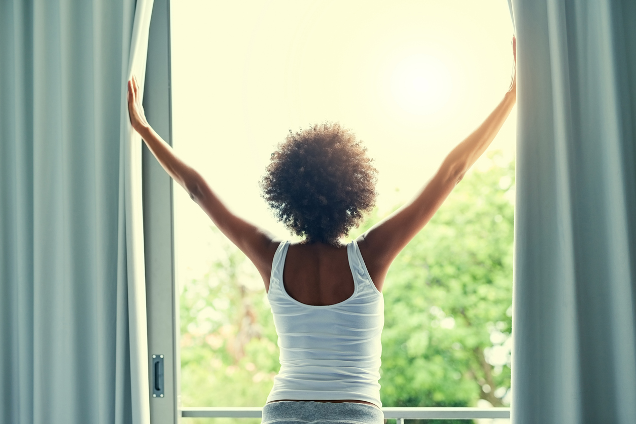 woman throws open curtains to sunlight to greet the day
