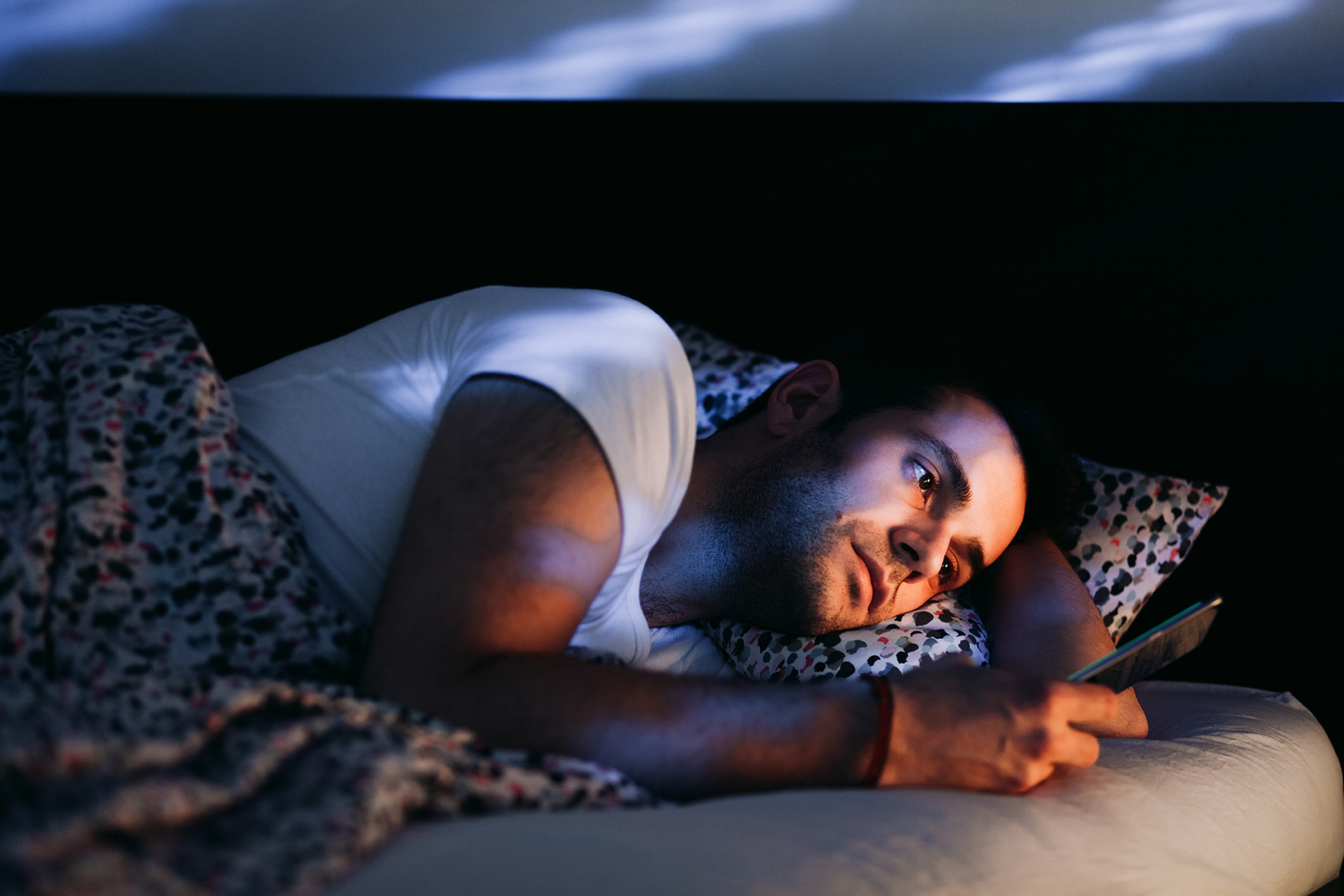 Young man uses his phone in bed in a dark bedroom