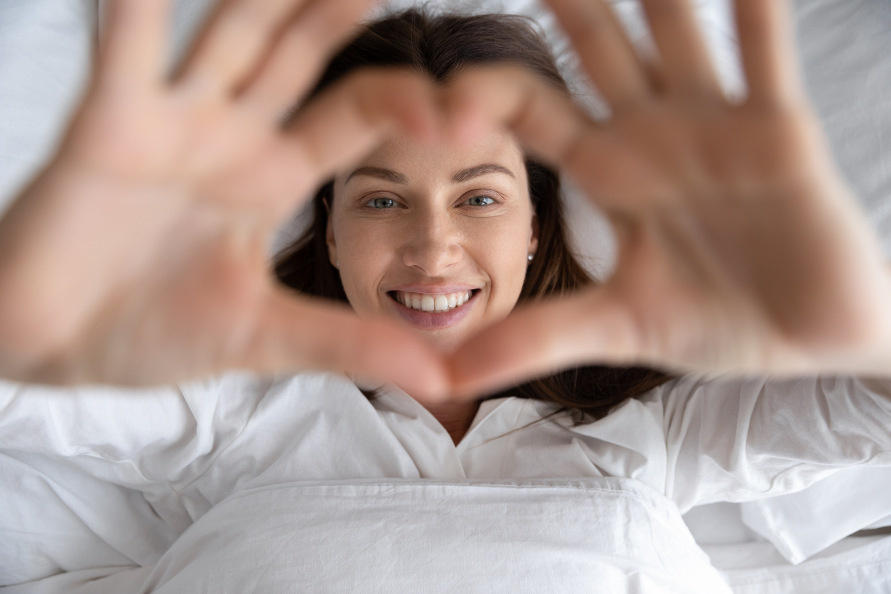 Woman holds up hands in heart shape in bed 