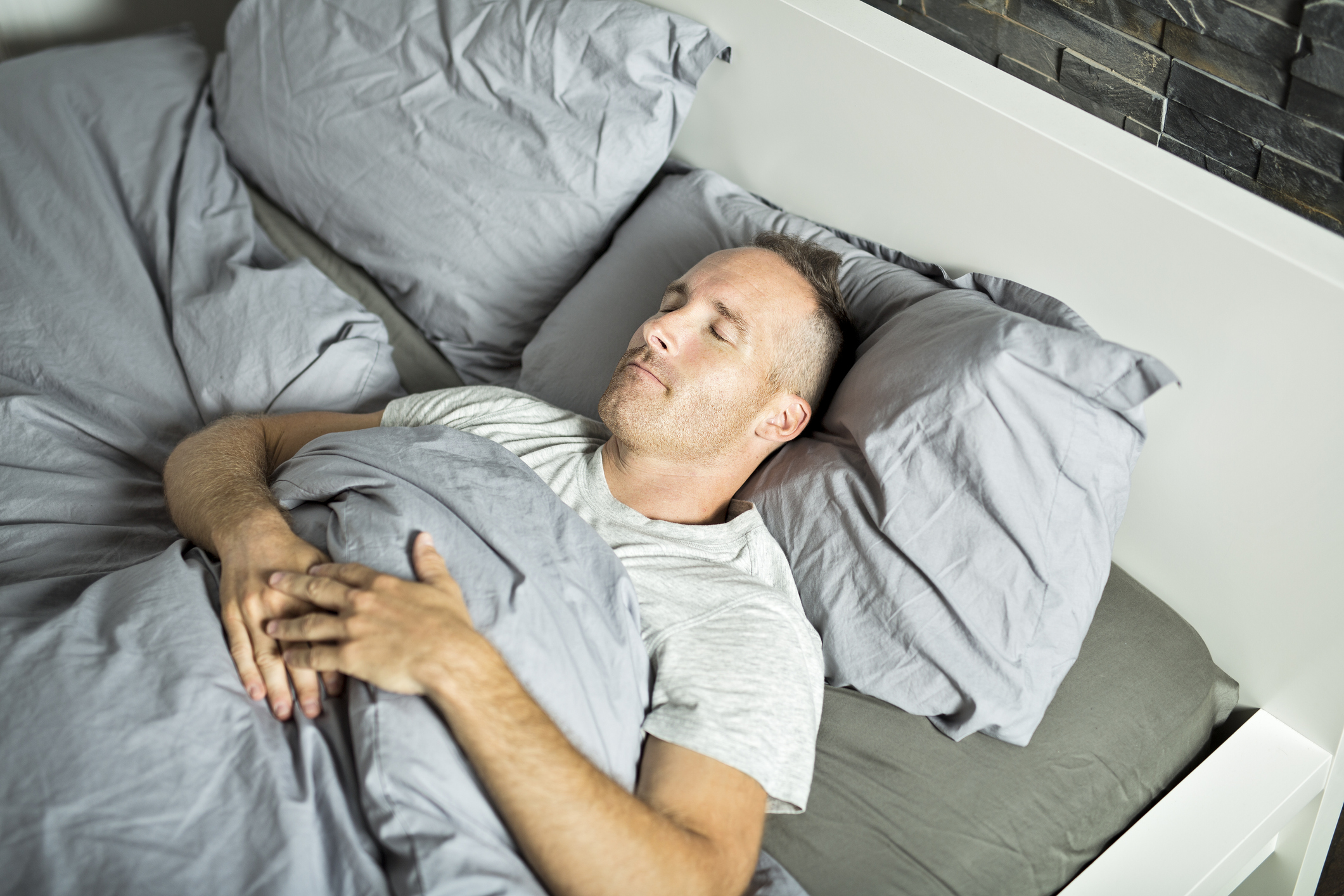 man sleeping on bad atop mattress with gray bedding 