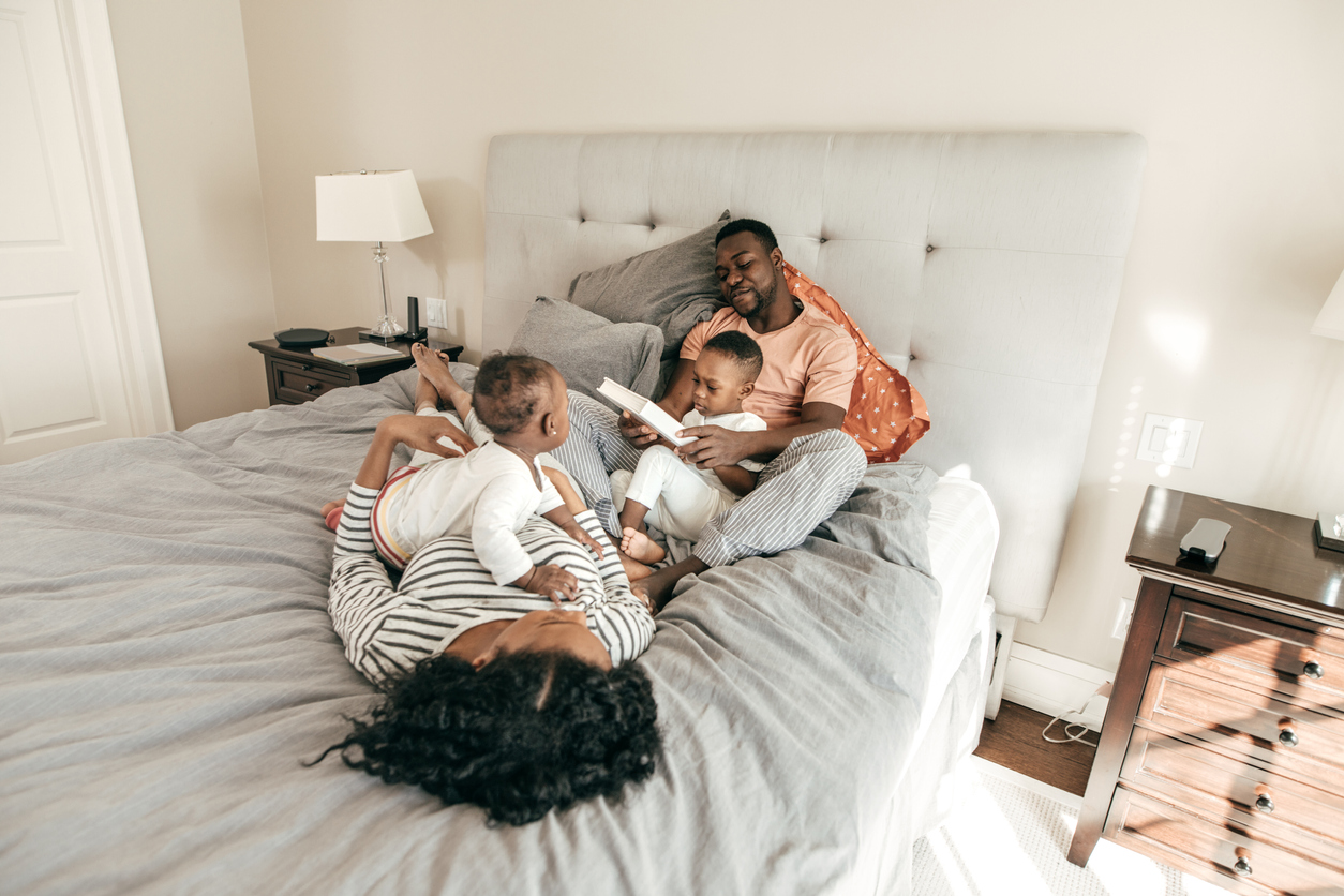 Mom, Dad, and two children snuggle and read stories in king size bed