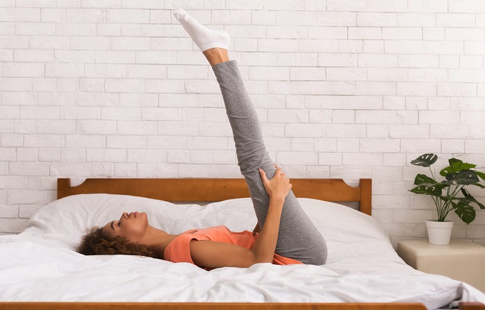 Woman stretching legs upright while laying on a bed