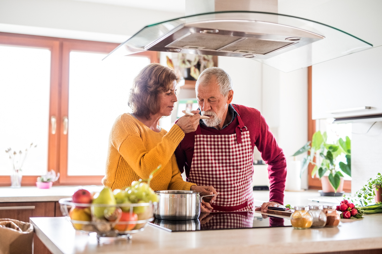 Husband and wife at a cooktop under a range hood in a bright kitchen