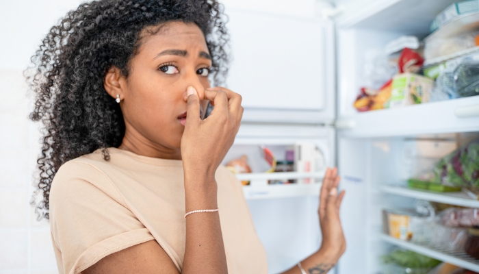 Woman plugging her nose because of the smell from the fridge