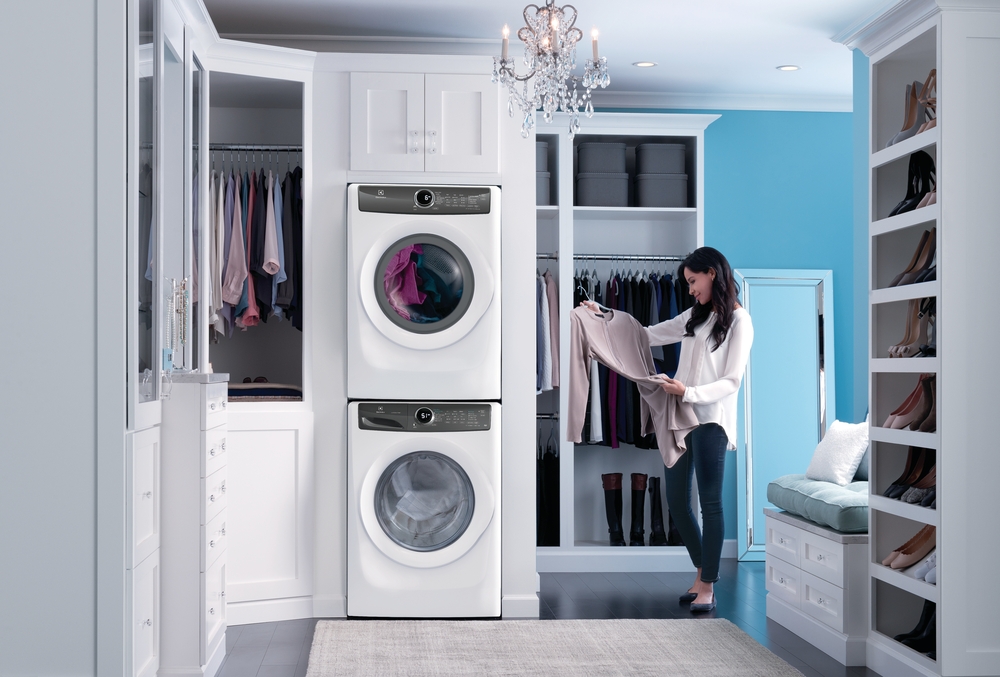 Woman holding sweatshirt next to Electrolux EFLW427UIW stacked washer and dryer