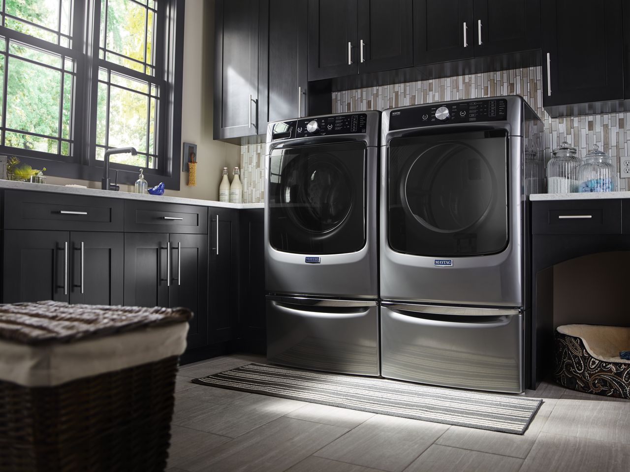 A set of Maytag laundry machines in a laundry room with dark cabinets