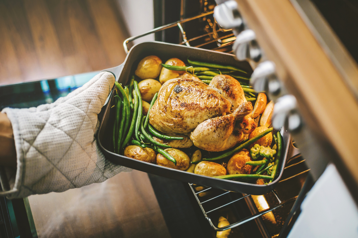 home cook places roasted turkey and vegetables into the oven