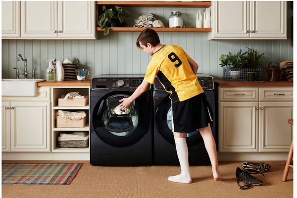 A young man uses the late-addition door to add clothing to his front load washer