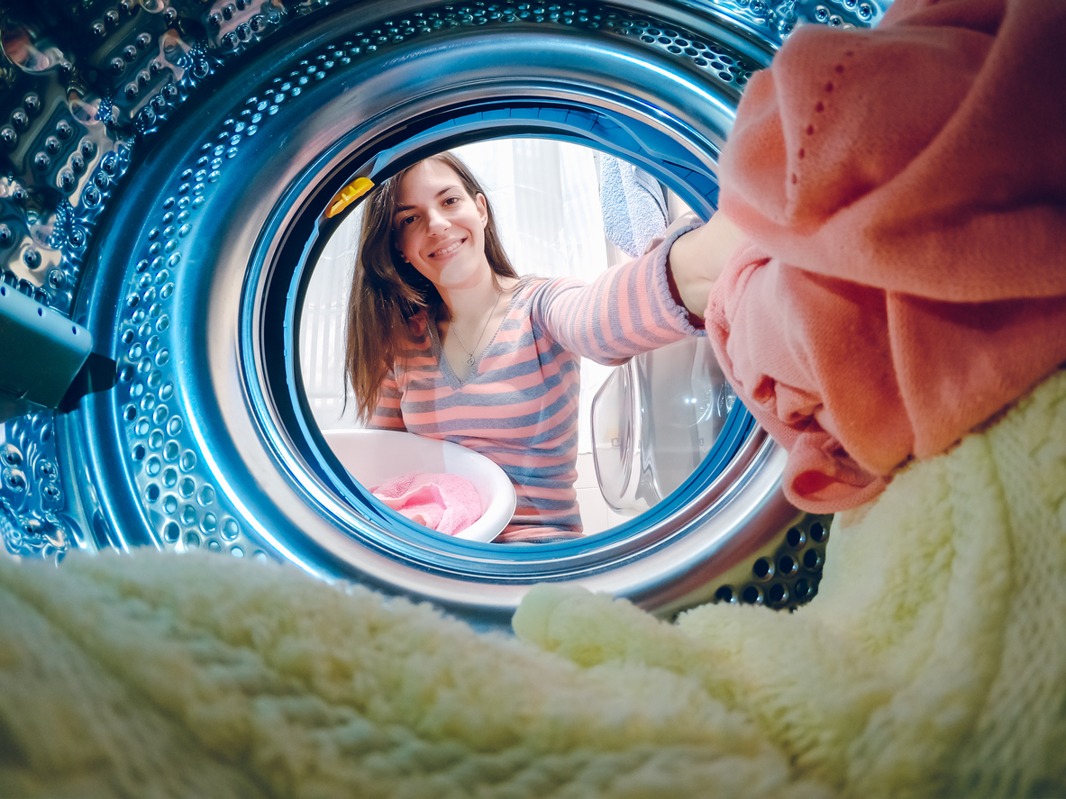 young woman putting laundry into dryer