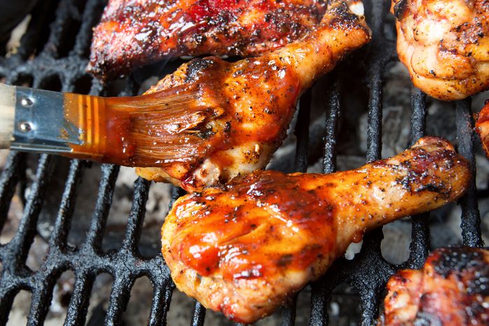 marinated chicken legs brushed with barbecue sauce on a charcoal grill
