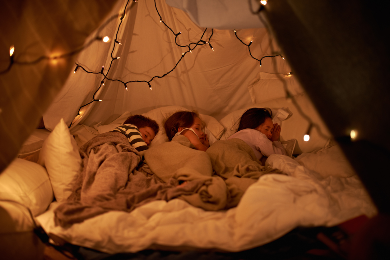 three kids sleeping in blanket fort