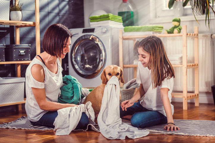 mother, daughter, and dog sorting clothes for washing in laundry room