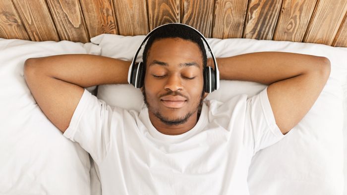 a calm man listens to a podcast as he lies in bed with headphones