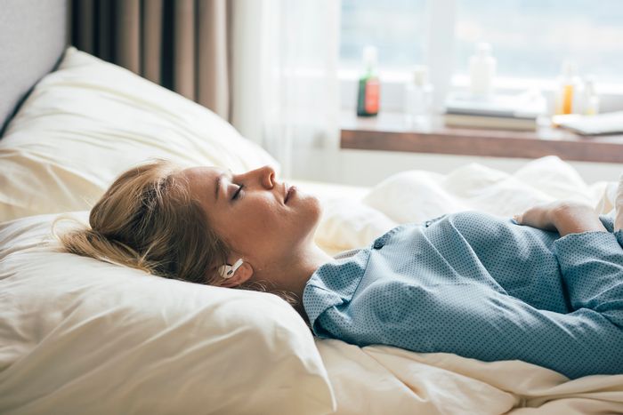 a relaxed woman lies in bed with wireless earbuds