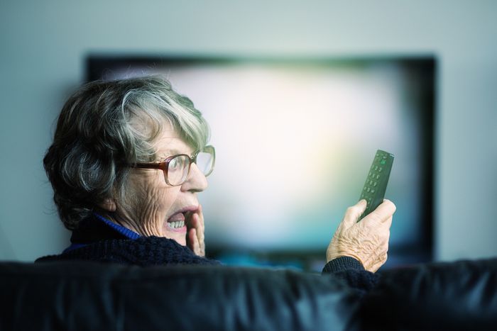 An older woman looks surprised at a television remote.