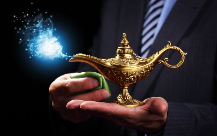 A man in a suit and tie holds a genie's lamp, polishing it with a green cloth. Magic smoke is coming out the end.