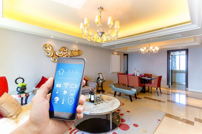 A hand holds out a smart phone in the foreground of an ornate living room.