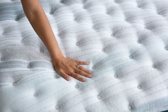 close view of an arm and hand pressing down on a plush white mattress top