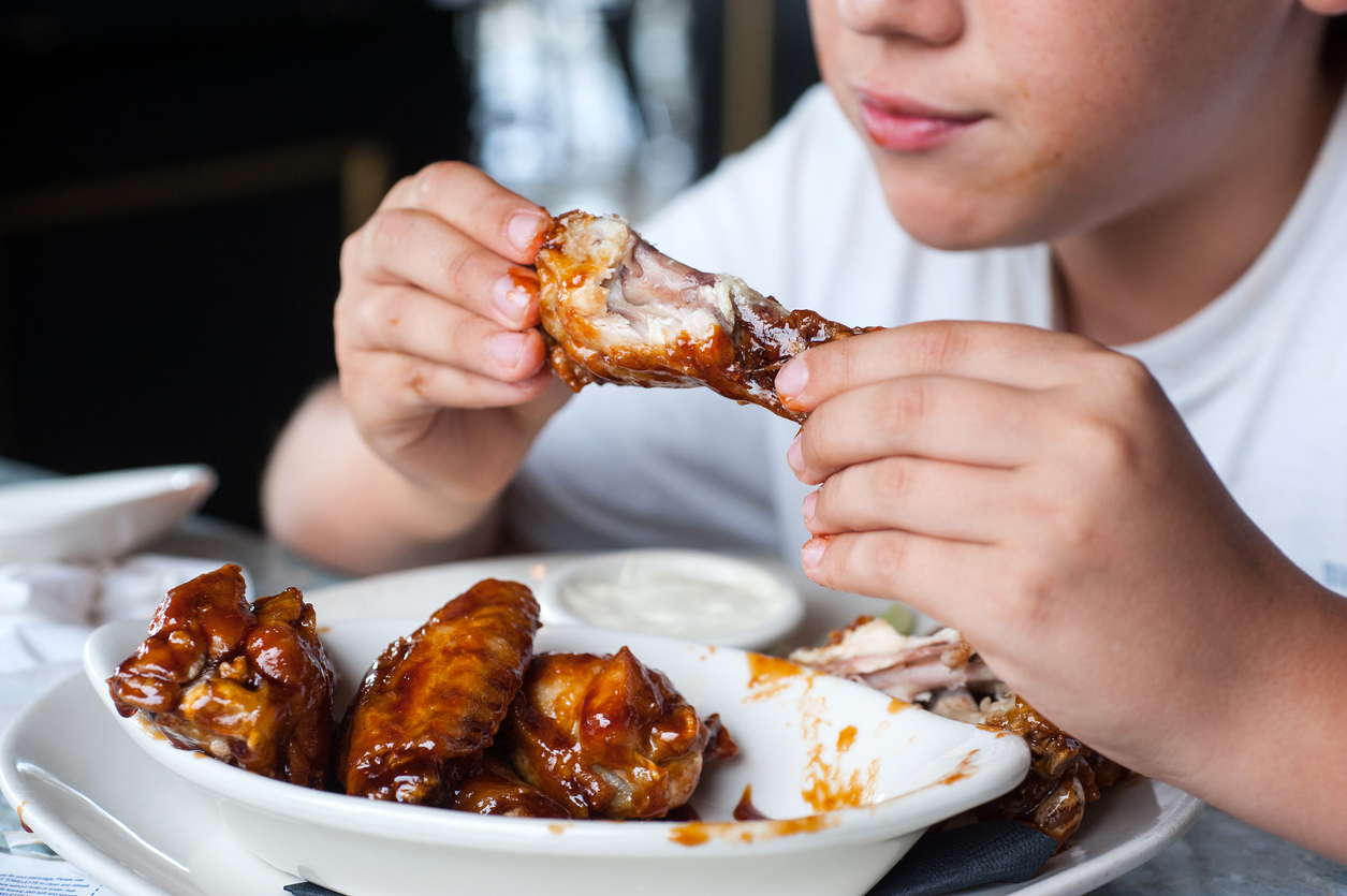 boy in white shirt eating bowl of barbecue wings